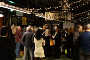 A large group of people in cocktail attire stand underneath white Christmas lights at the 2023 Silver Jubilee.